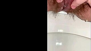 Chlupatá kunda mladé ženy čůrá ve sprše, stříká po bílých stehnech